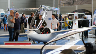 Besucher am SZD-Stand der AERO 2024 neben einem geöffneten Segelflugzeug-Cockpit.